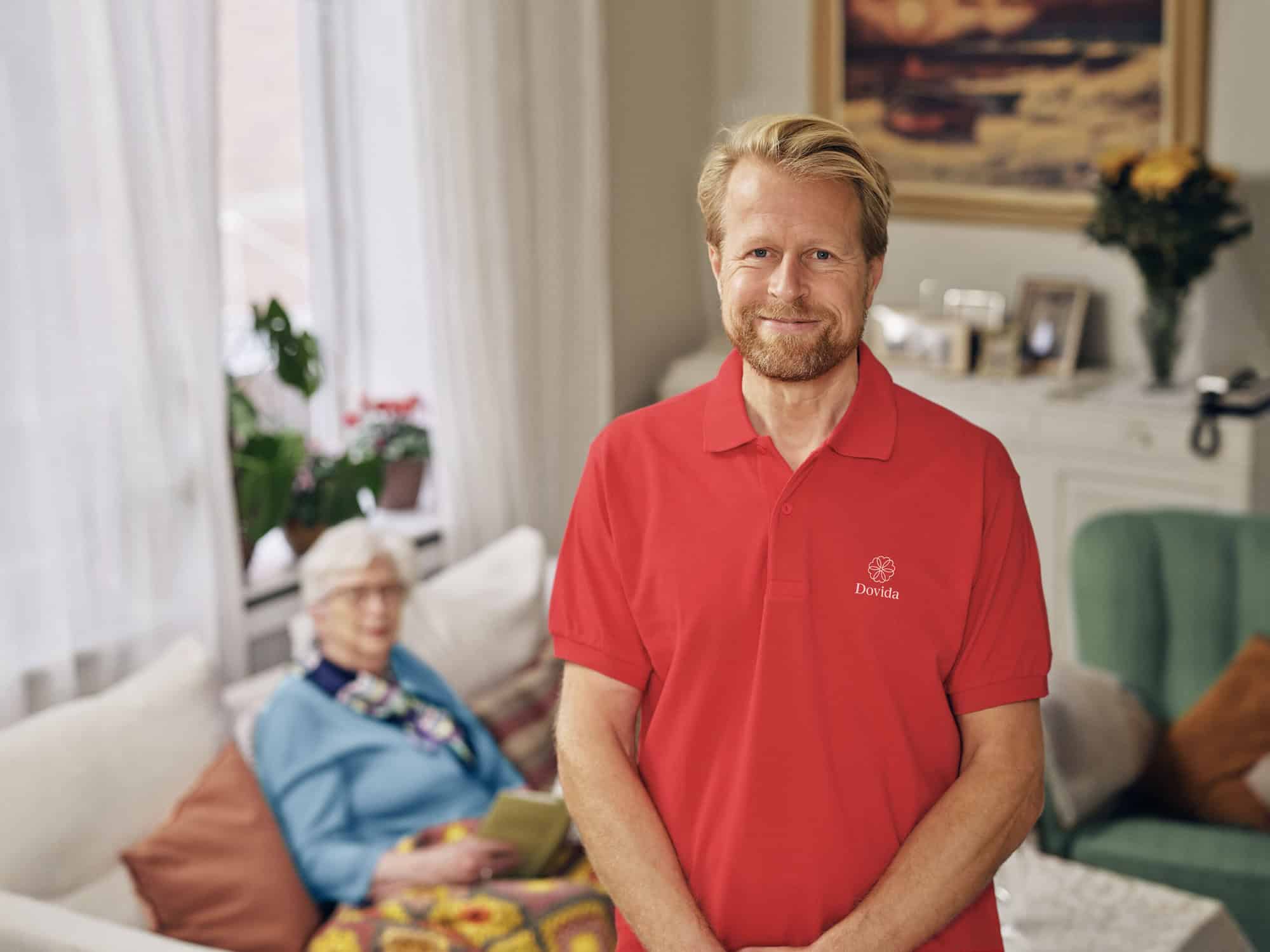 Betreuungskraft im roten Dovida-T-Shirt steht selbstbewusst da und symbolisiert die offene Atmosphäre bei Dovida Karriere.